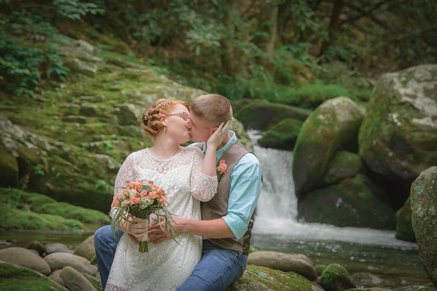 A romantic moment shared between a couple near a tranquil forest waterfall surrounded by moss-covered rocks in Pigeon Forge.