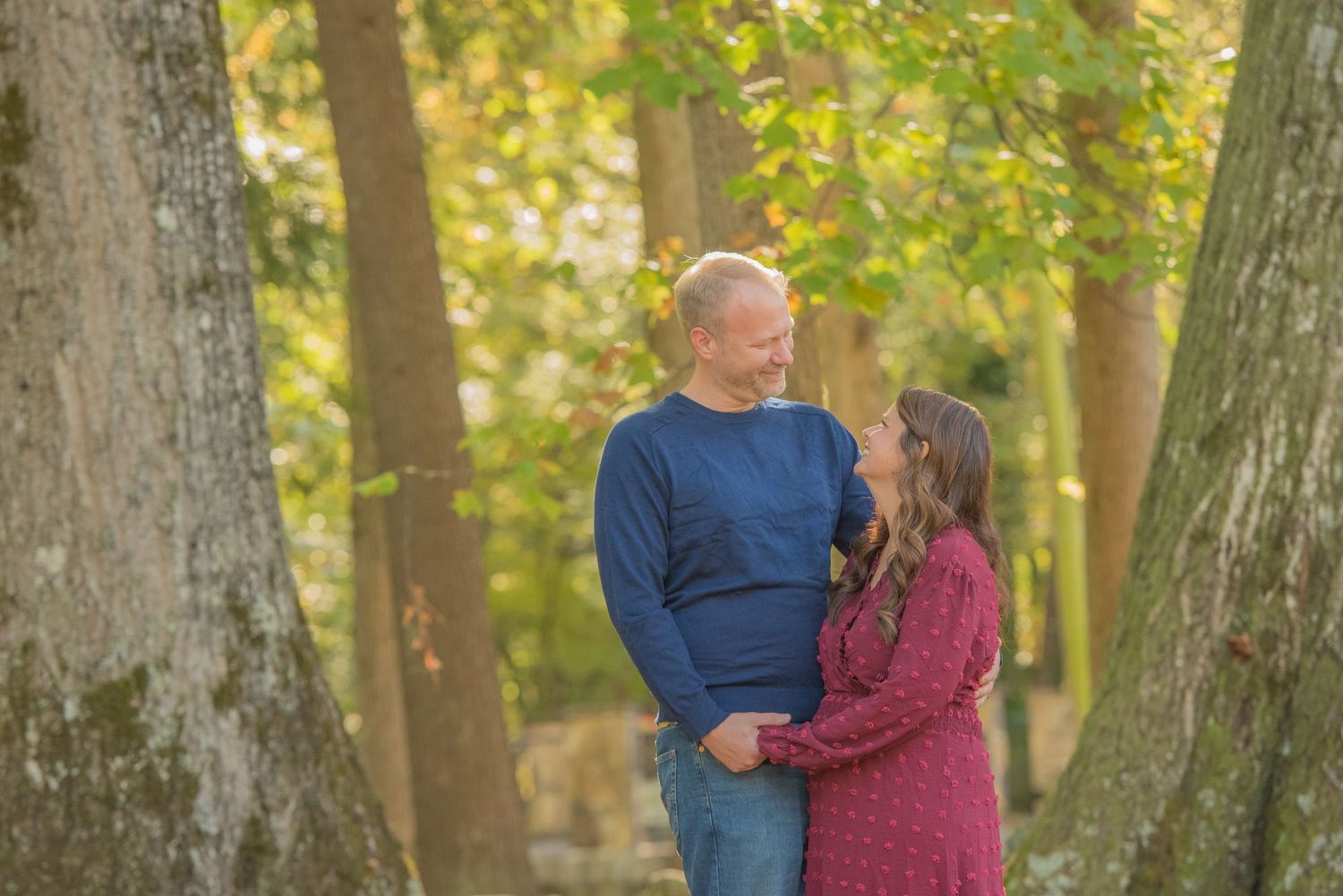 An engagement couple romantic mature couple embraces between two large trees in a sunlit autumn forest setting by Townsend Photographers.