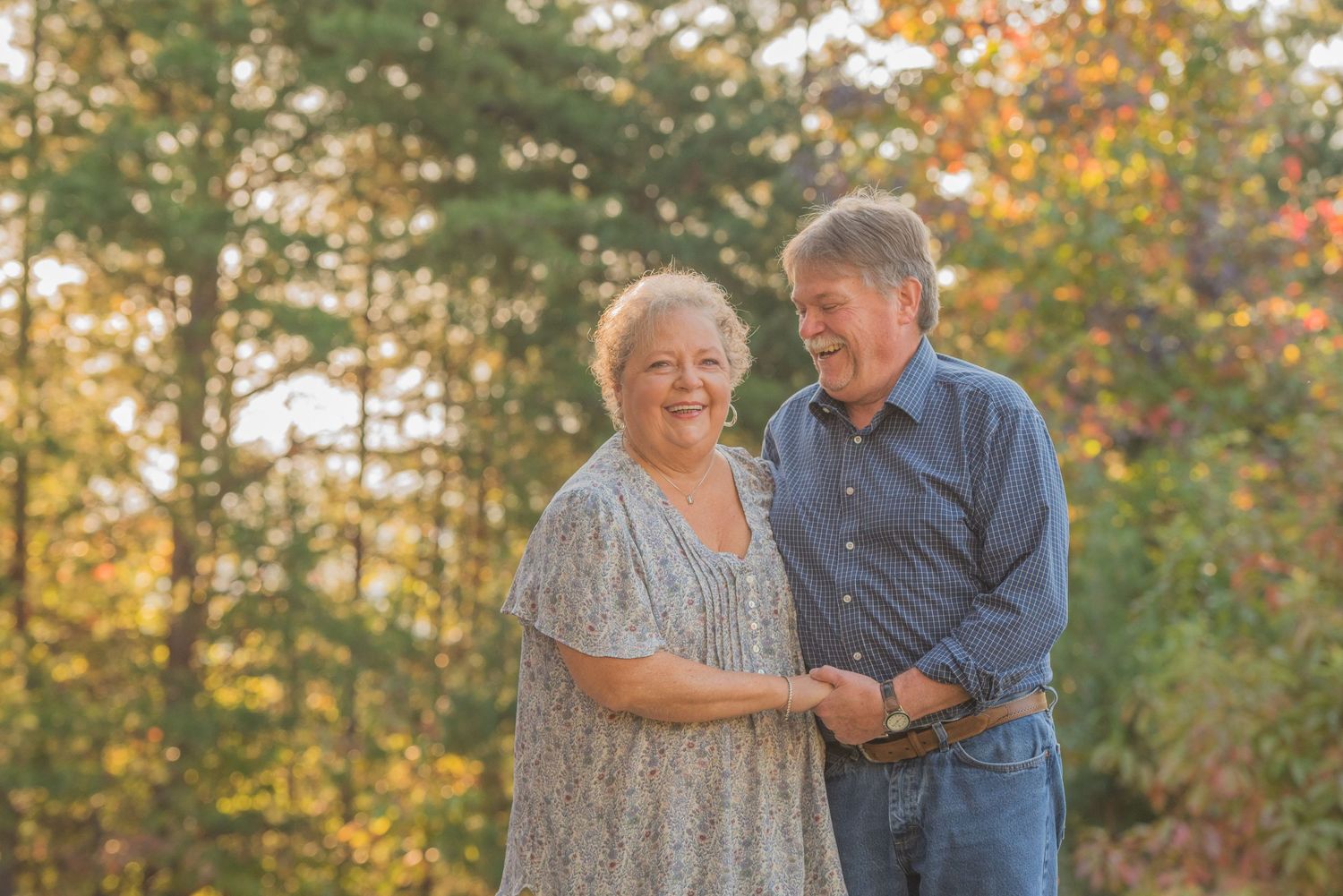 Senior couple sharing a warm moment together outside during golden hour with autumn trees in the background by Sevierville TN Photographers.