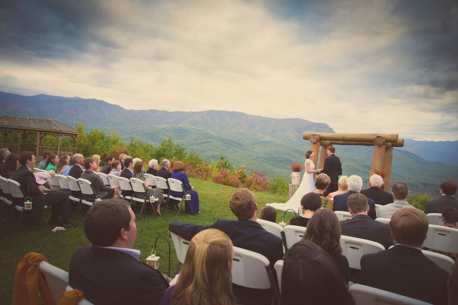 An outdoor mountain wedding ceremony takes place under a wooden arch with guests seated overlooking scenic valley views in Gatlinburg TN.