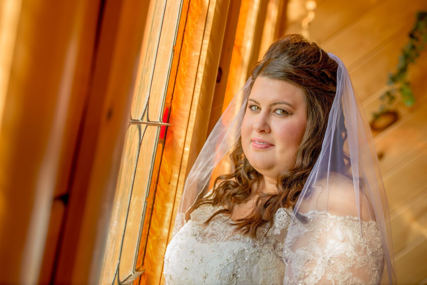 Pigeon Forge Wedding Photographers portrait of a bride in a white lace wedding dress and veil poses by a warmly lit window.