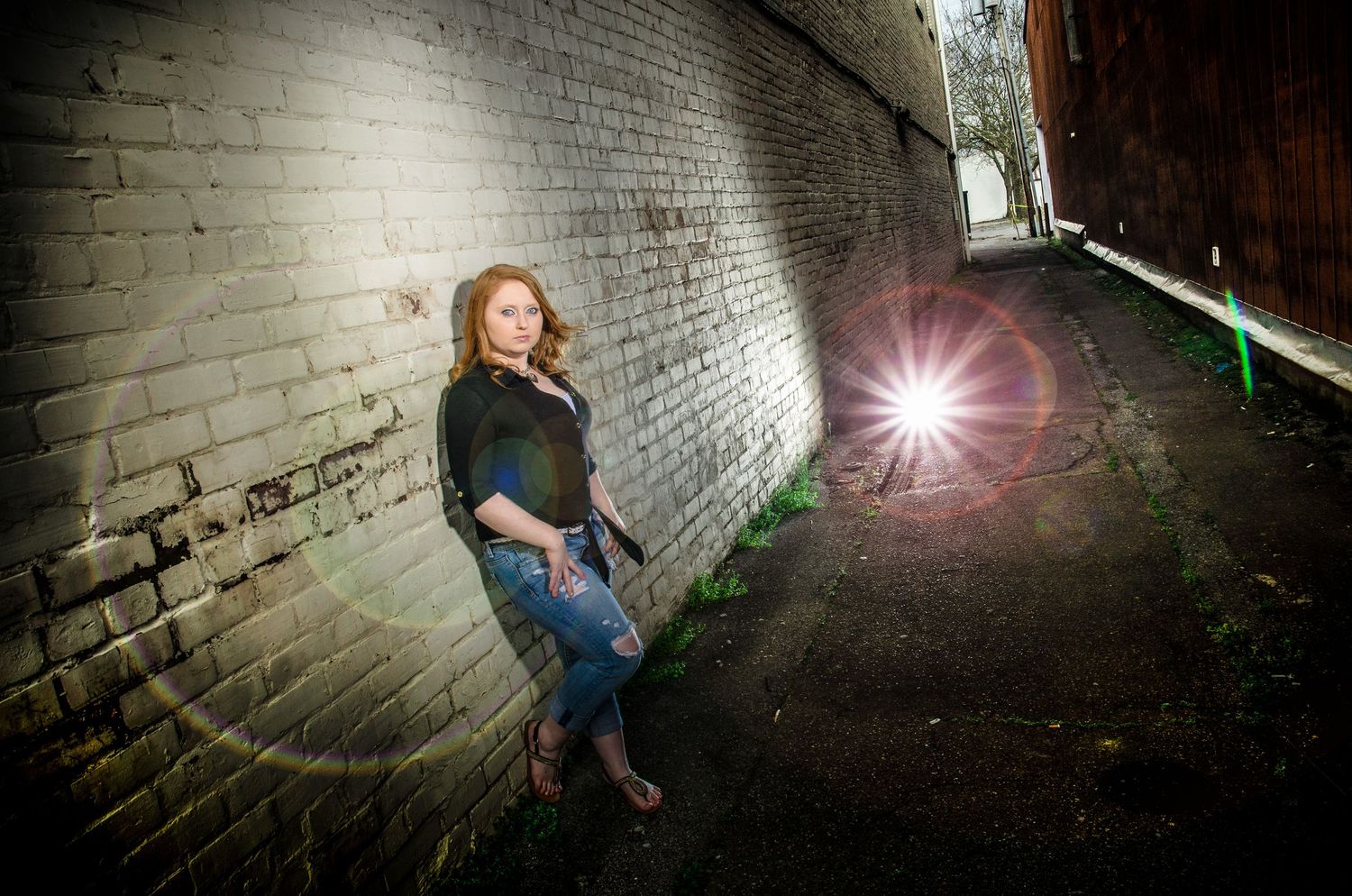 A person leans against a white brick wall in a dark tunnel while a bright light flare appears in the distance.