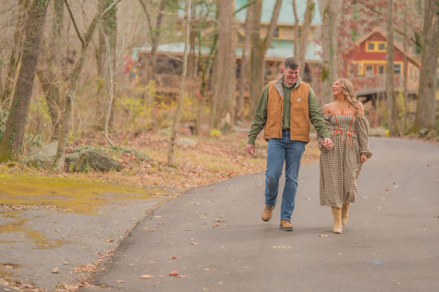 Two people take an autumn stroll down a wooded path with fall leaves and rustic cabins in the background by Gatlinburg TN Photographers.