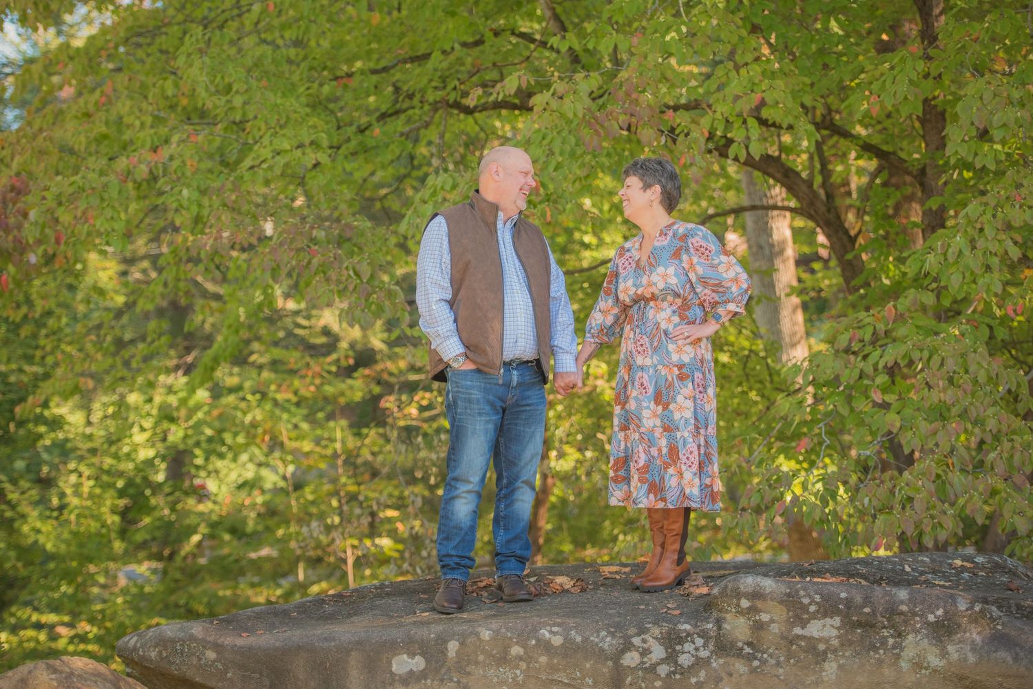 Two older people standing together on a large rock in a lush green forest during golden hour by Gatlinburg Photographers.