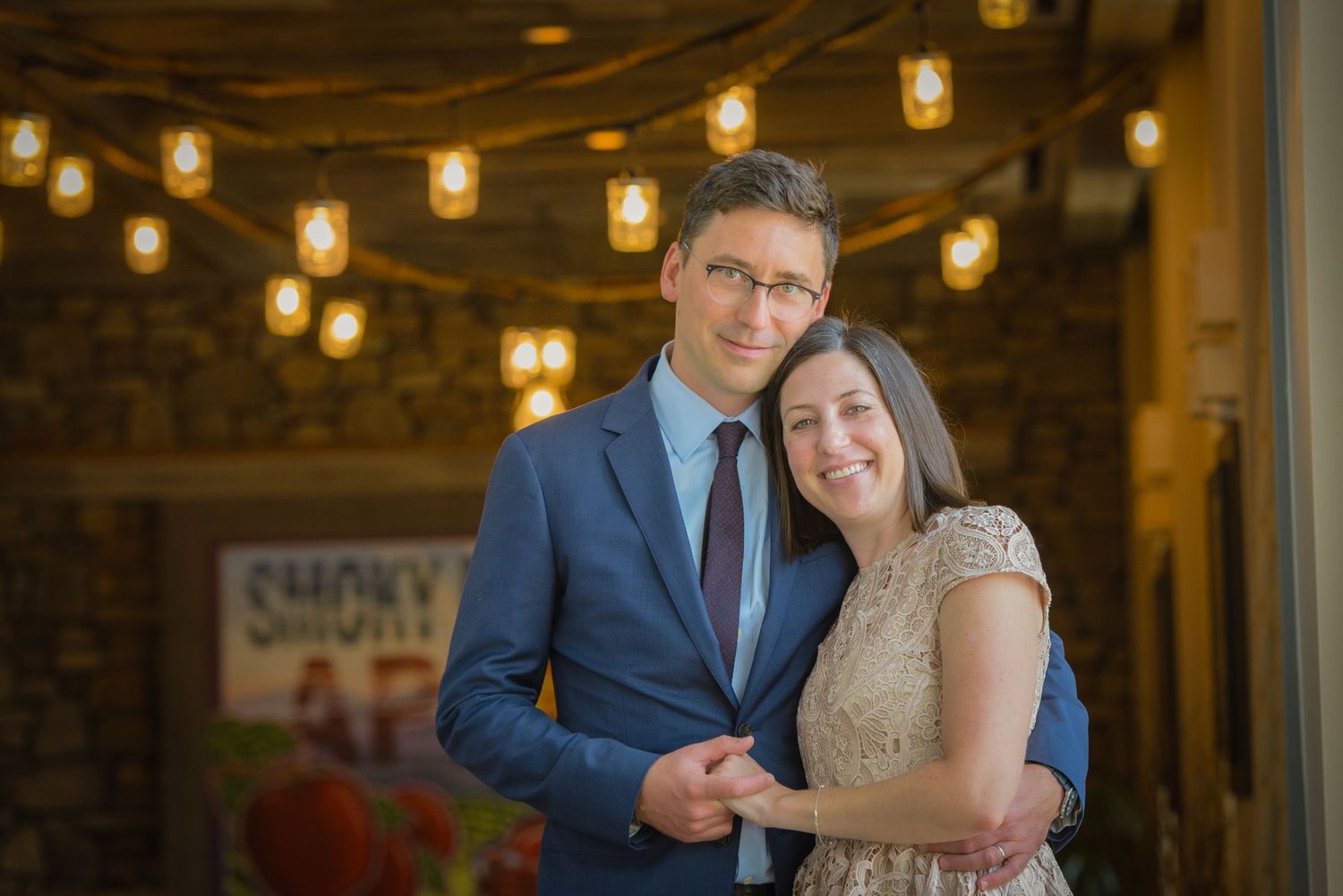 A couple embraces at their wedding with string lights glowing warmly in the background by Sevierville TN Photographers.