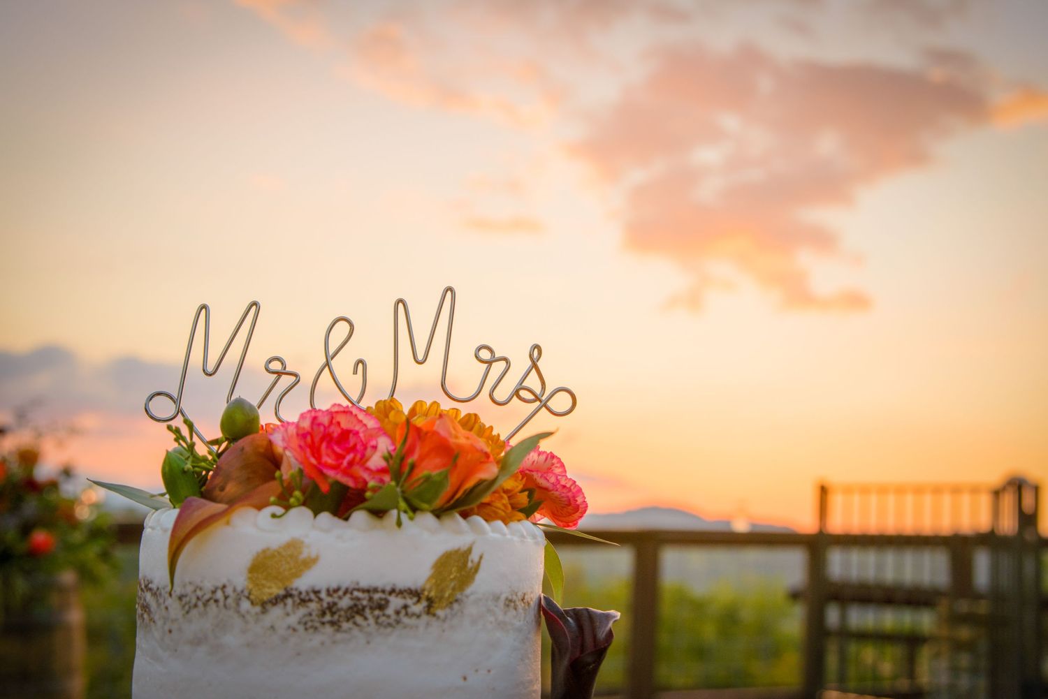 Wedding cake with Mr and Mrs topper decorated with colorful flowers against a sunset sky during outdoor reception in Gatlinburg TN.
