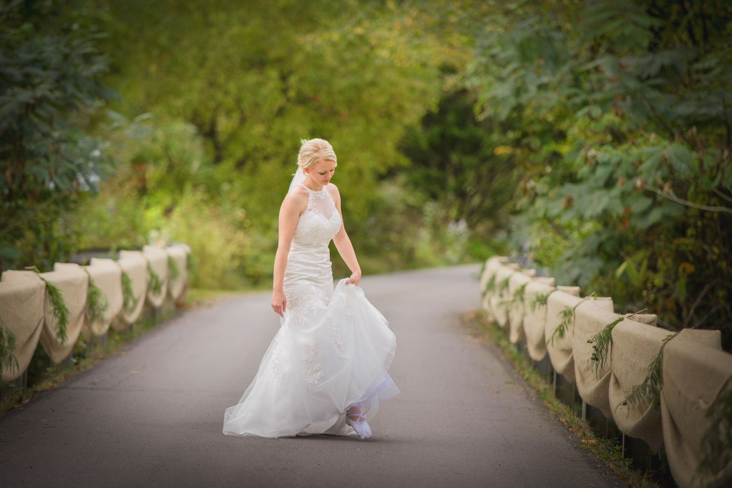 A bride in a flowing white lace gown poses on a garden pathway with stone railings and greenery in the background in Pigeon Forge.