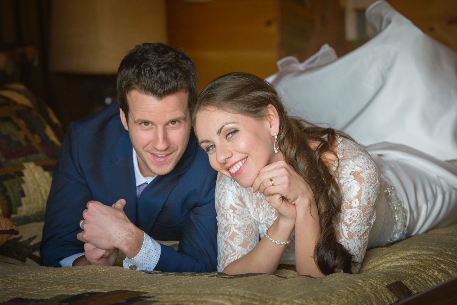 A couple in wedding attire lies together on a couch, the bride in lace and the groom in navy blue in Newport TN.