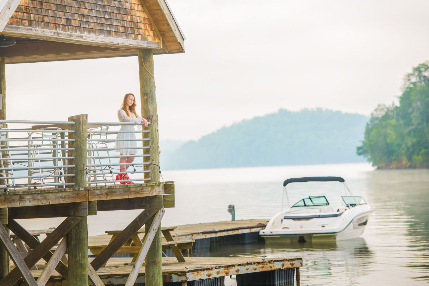 A rustic lake dock with covered shelter and moored motorboat against misty mountain backdrop.