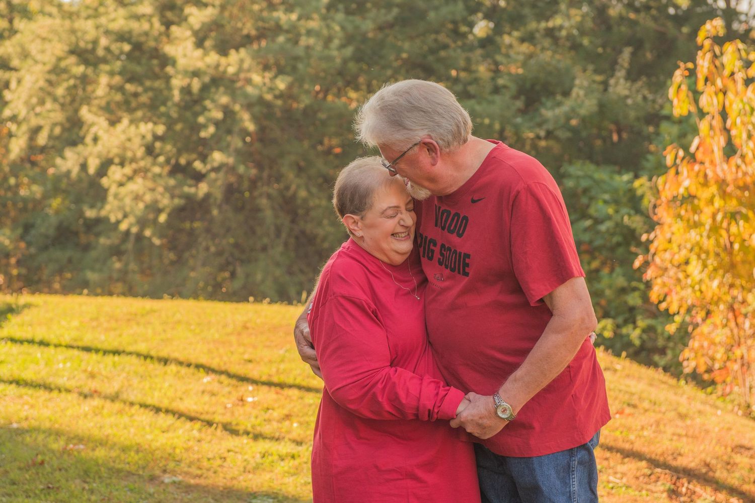 Loving anniversary couple in matching red shirts embrace outdoors during golden autumn sunset in a park setting by Sevierville Photographers