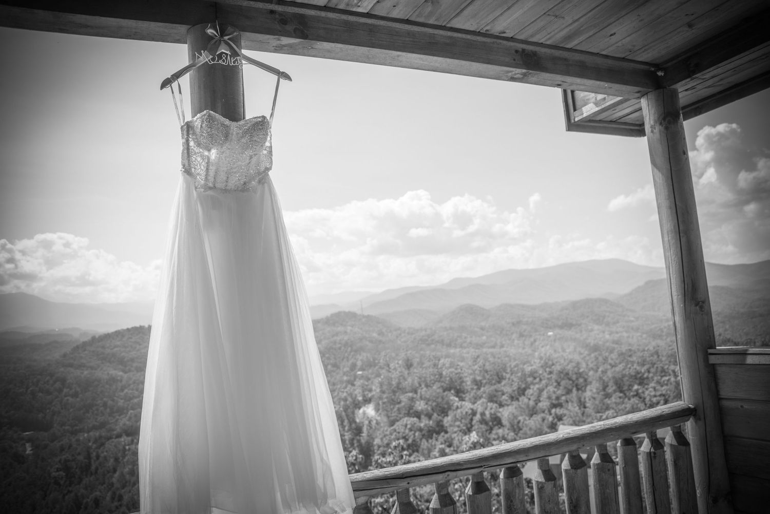 Wedding dress hangs from rustic porch railing against scenic mountain vista in black and white photography in Pigeon Forge Wedding.