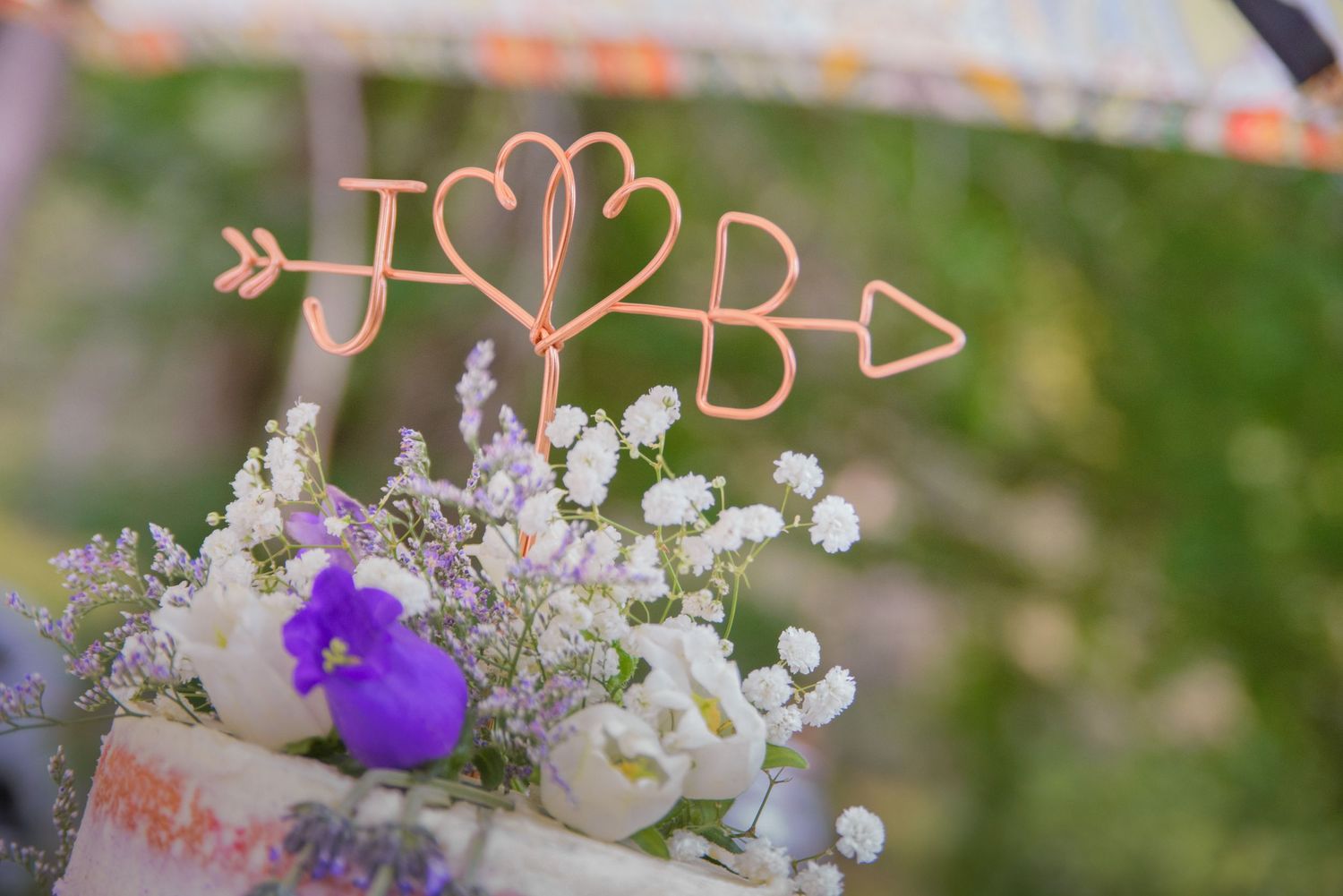 Decorative gold wire initials with hearts sit atop a floral arrangement of purple and white flowers by Morristown Wedding Photographers.