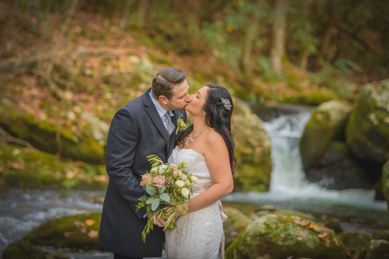Pigeon Forge Wedding Photographers portrait of a romantic wedding couple embraces near a cascading forest waterfall.