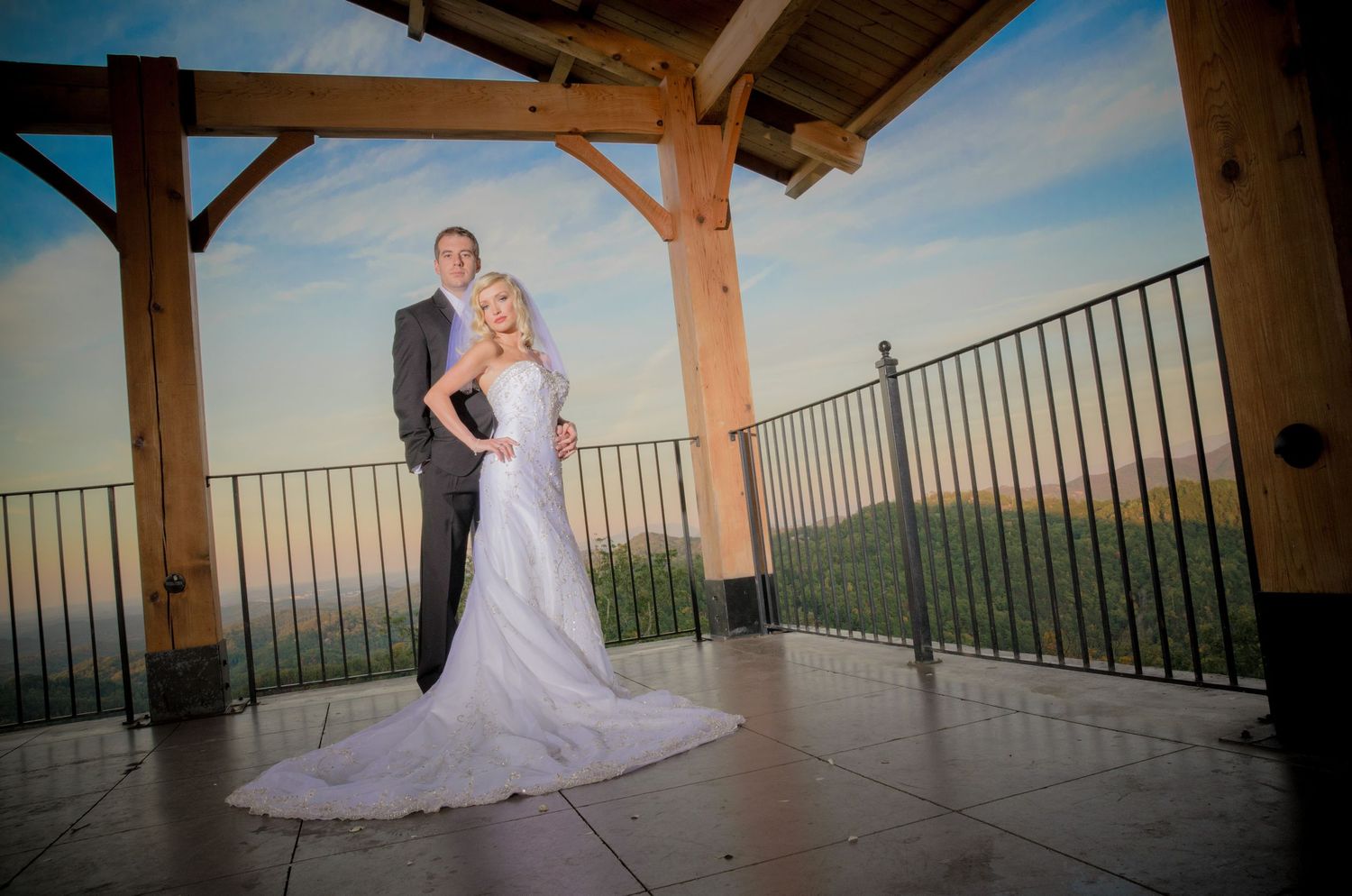 A couple in formal wedding attire embrace under a wooden pavilion overlooking mountain views at sunset by Gatlinburg Wedding Photographers.