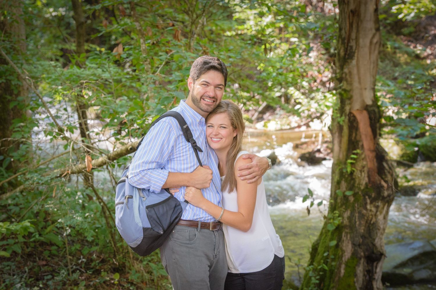 A couple poses together on a hiking trail near a rushing stream in a lush forest setting by Pigeon Forge Photographer tn.