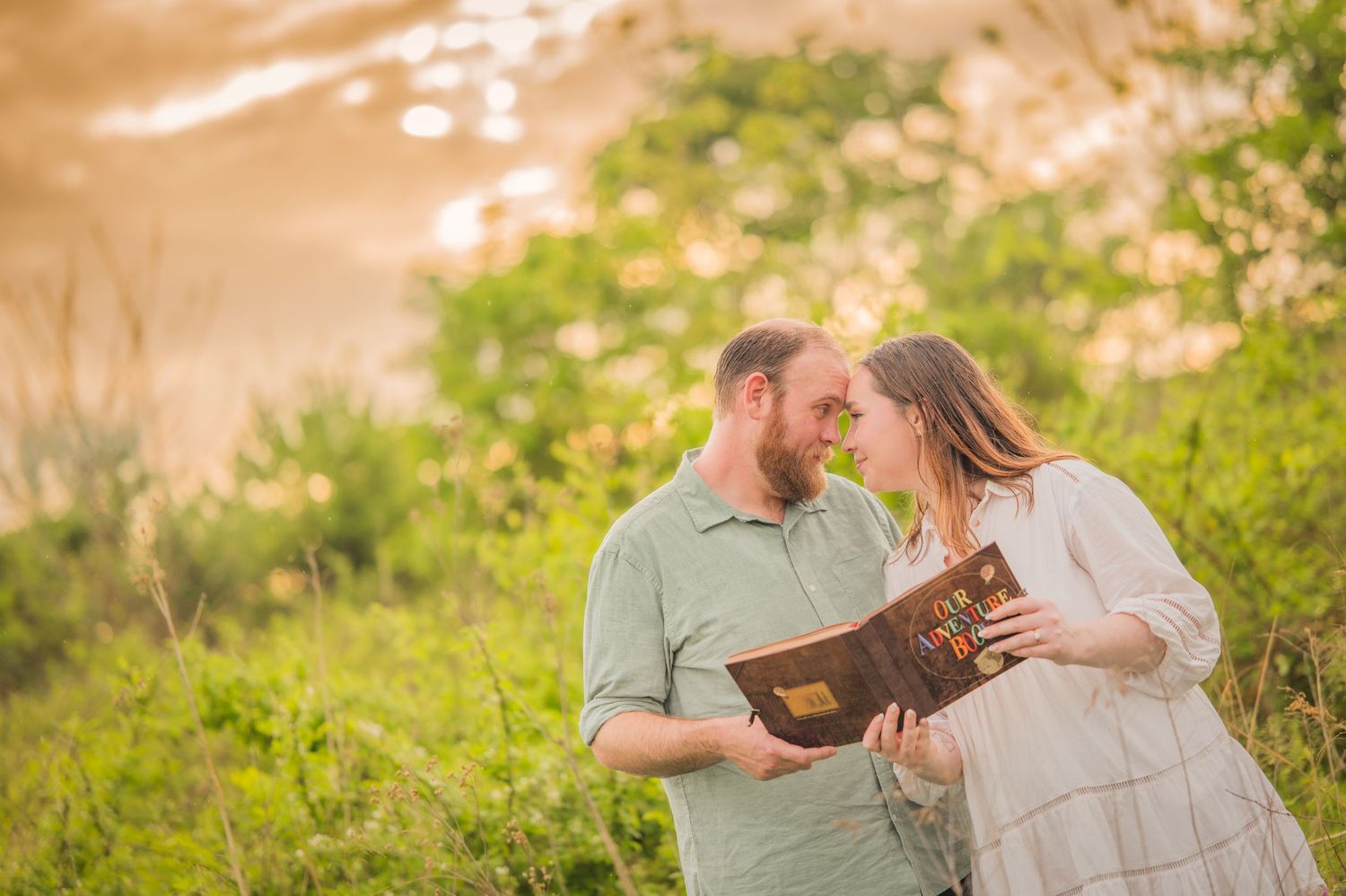 A couple shares an intimate moment while holding a book together in a sunlit field with green foliage by Gatlinburg Photographers TN.
