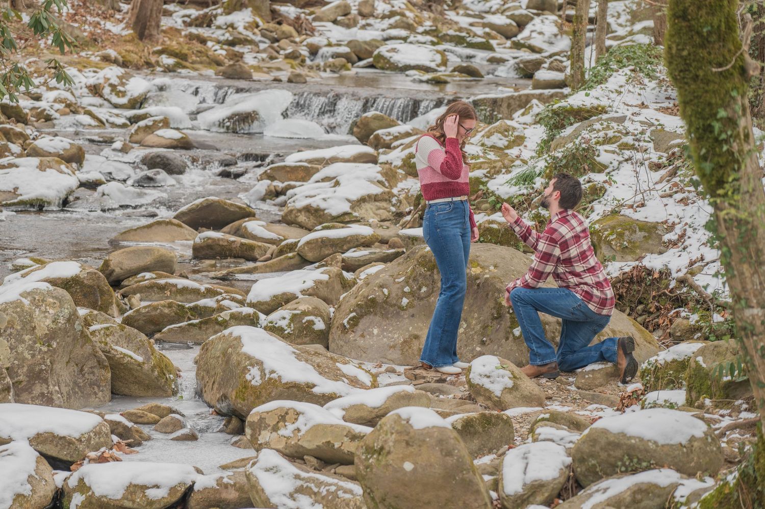 Two people exploring a snowy winter landscape with rocky terrain along a mountain stream in nature by Gatlinburg TN Photographers.