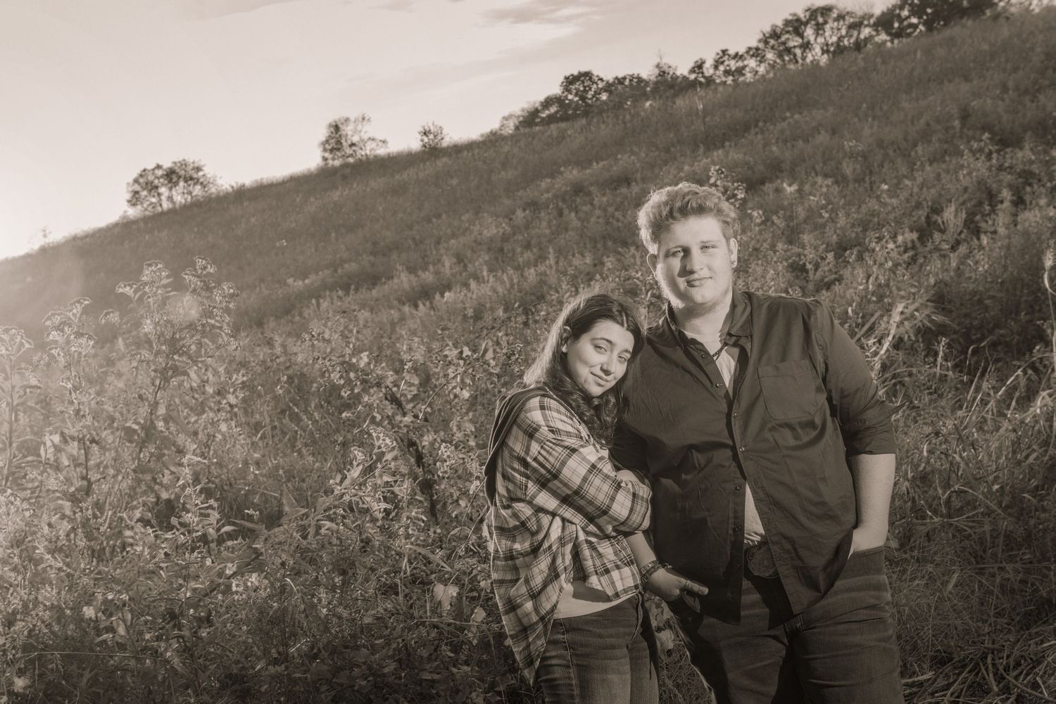 A vintage black and white photograph showing a couple embracing on a hillside with trees in the background by Sevierville Photographer.
