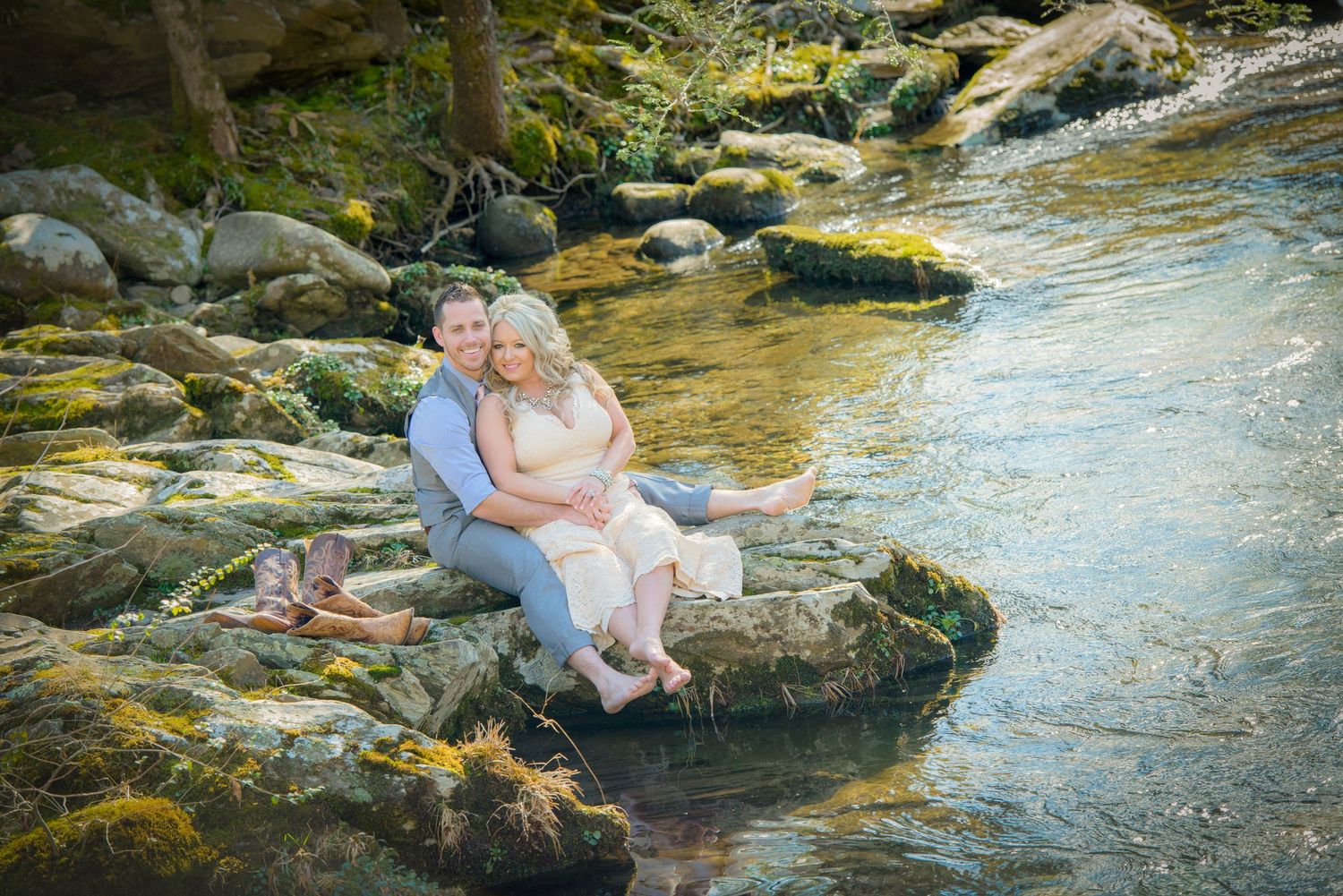 A couple sits peacefully together on a mossy rock by a flowing mountain stream in a scenic woodland setting by Gatlinburg Weddings.