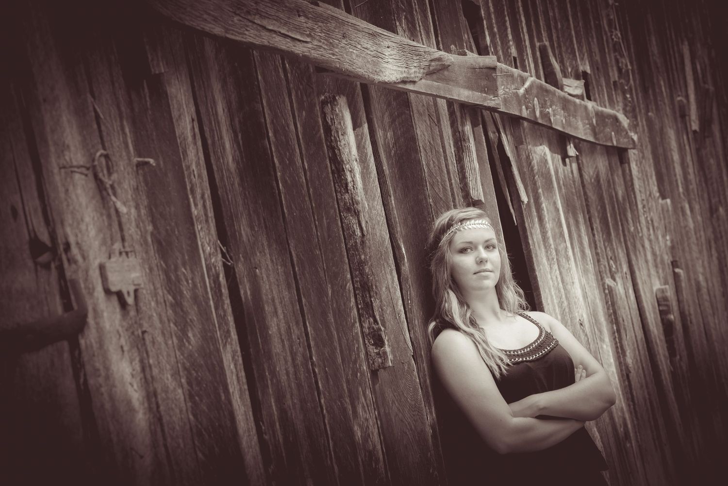 Black and white portrait of a person standing with crossed arms against a rustic wooden wall.