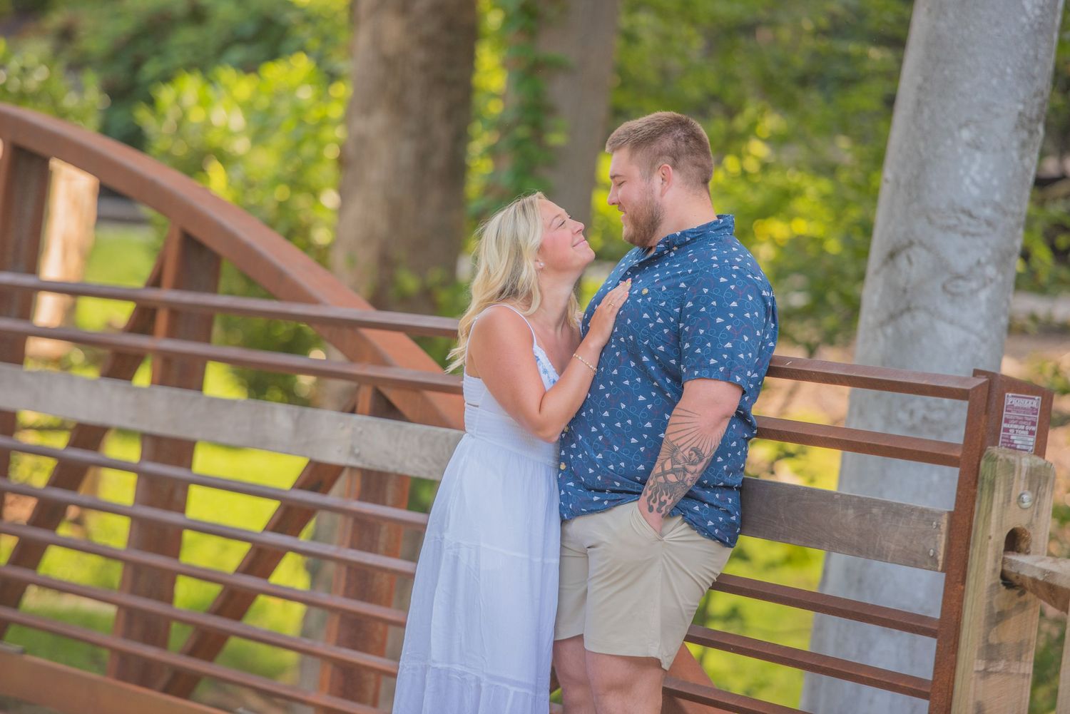 A couple shares an intimate moment on a wooden bridge surrounded by lush greenery on a sunny day by Sevierville TN Photographer.