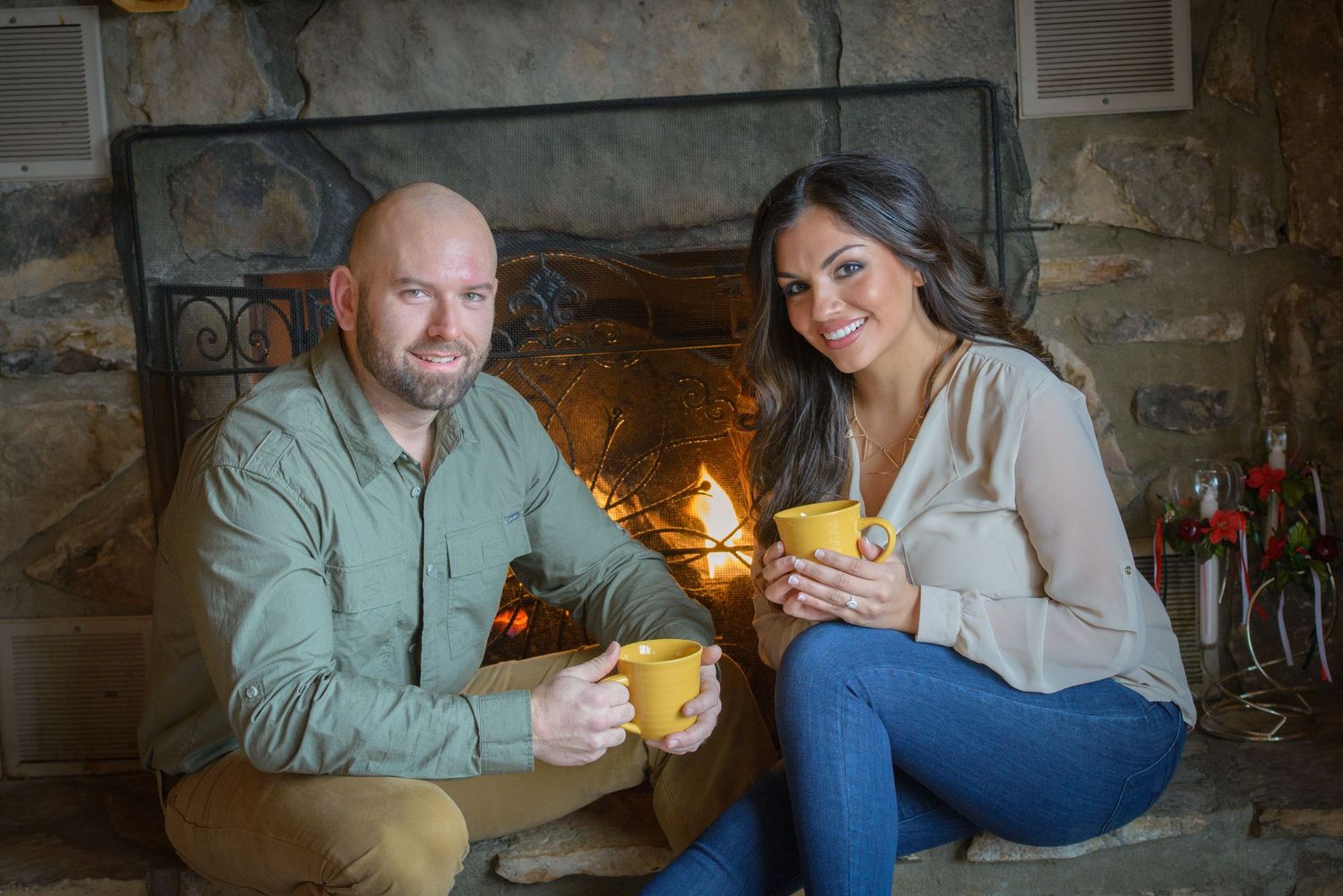 Two people sit by a cozy fireplace drinking coffee in mugs on a winter evening at their cabin rental in Pigeon Forge.