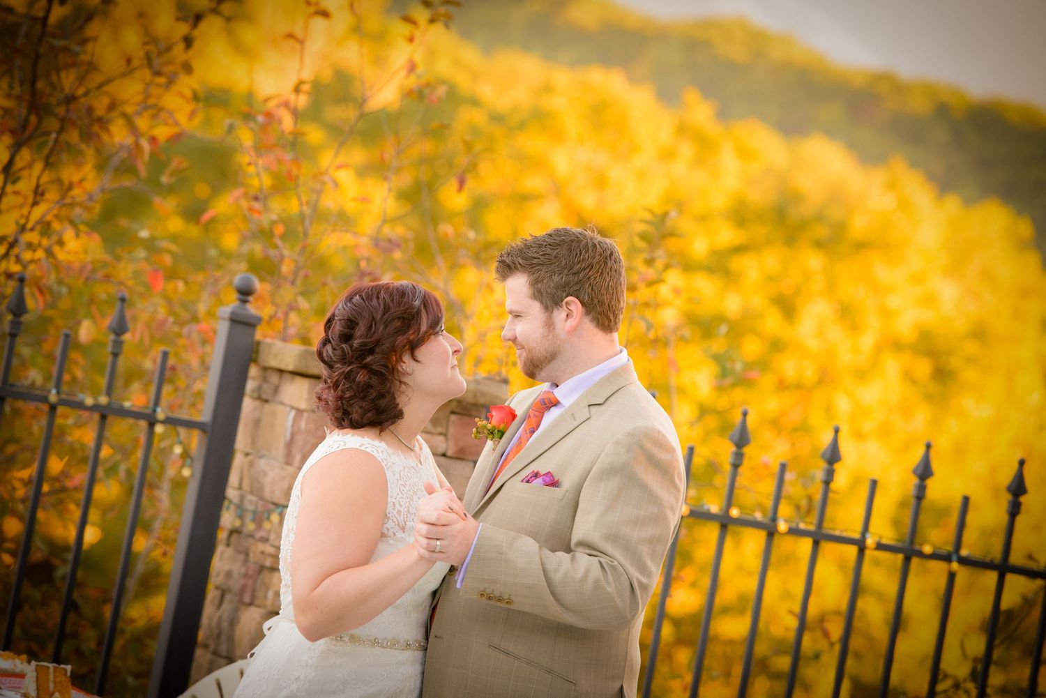 A romantic autumn wedding moment captured against vibrant yellow foliage and decorative iron fencing by Gatlinburg TN Wedding Photographers.