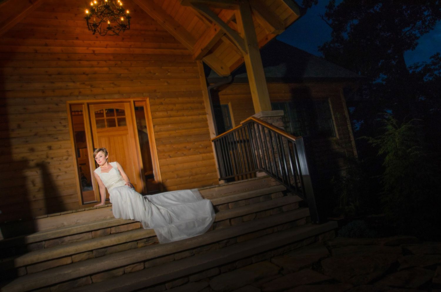 A bride in a flowing white dress sits on wooden steps of a rustic cabin at night with dramatic lighting in Morristown TN.