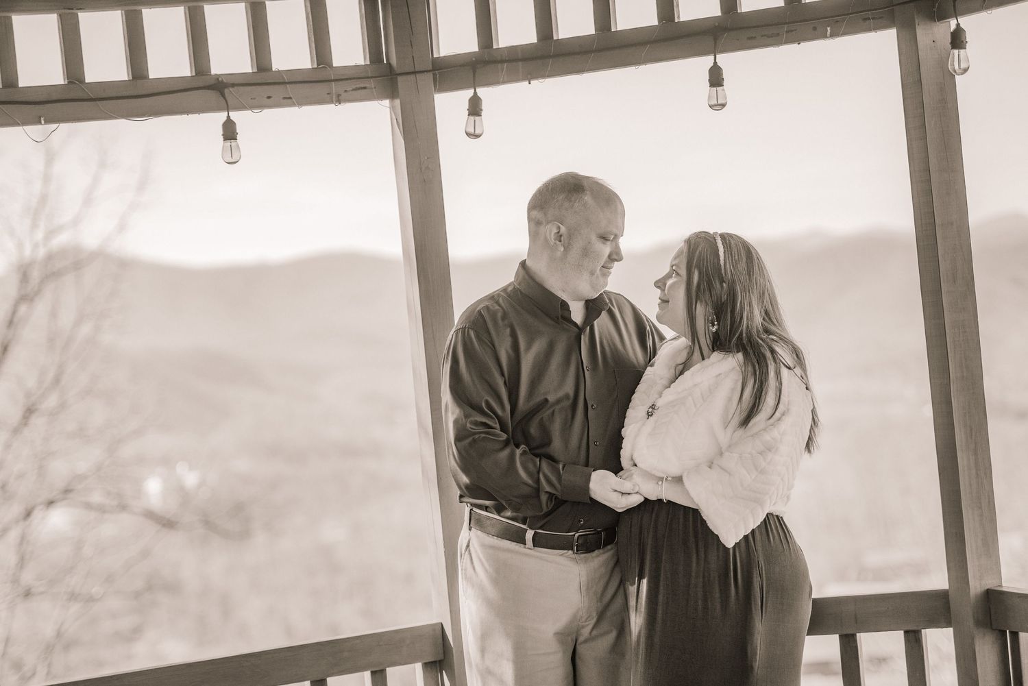 A couple shares a tender moment while standing on a porch overlooking a scenic landscape in black and white by Pigeon Forge Photographer tn.