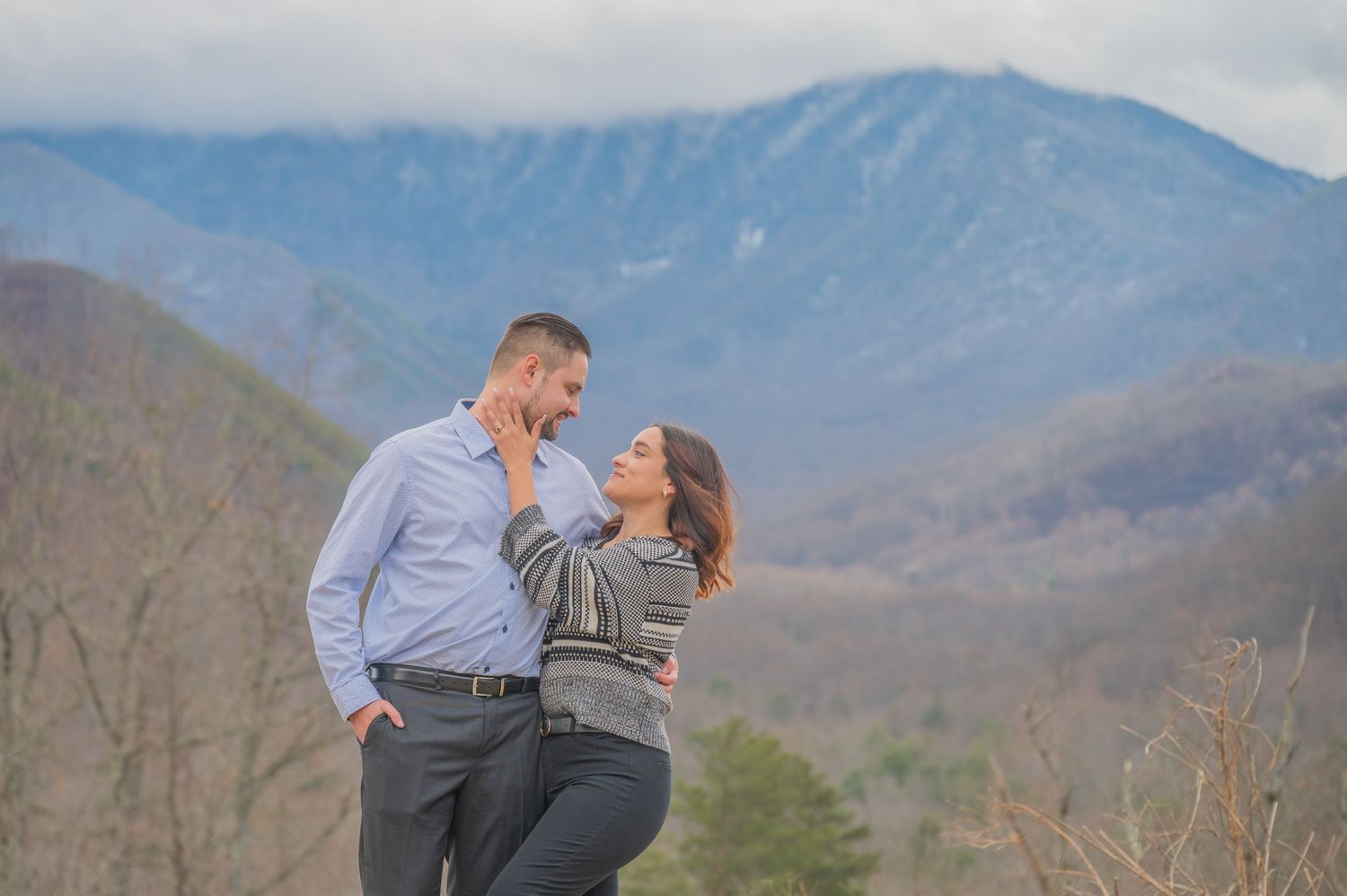 A couple share an intimate moment while standing on a mountain overlook with misty blue ridge mountains by Pigeon Forge Photographers.