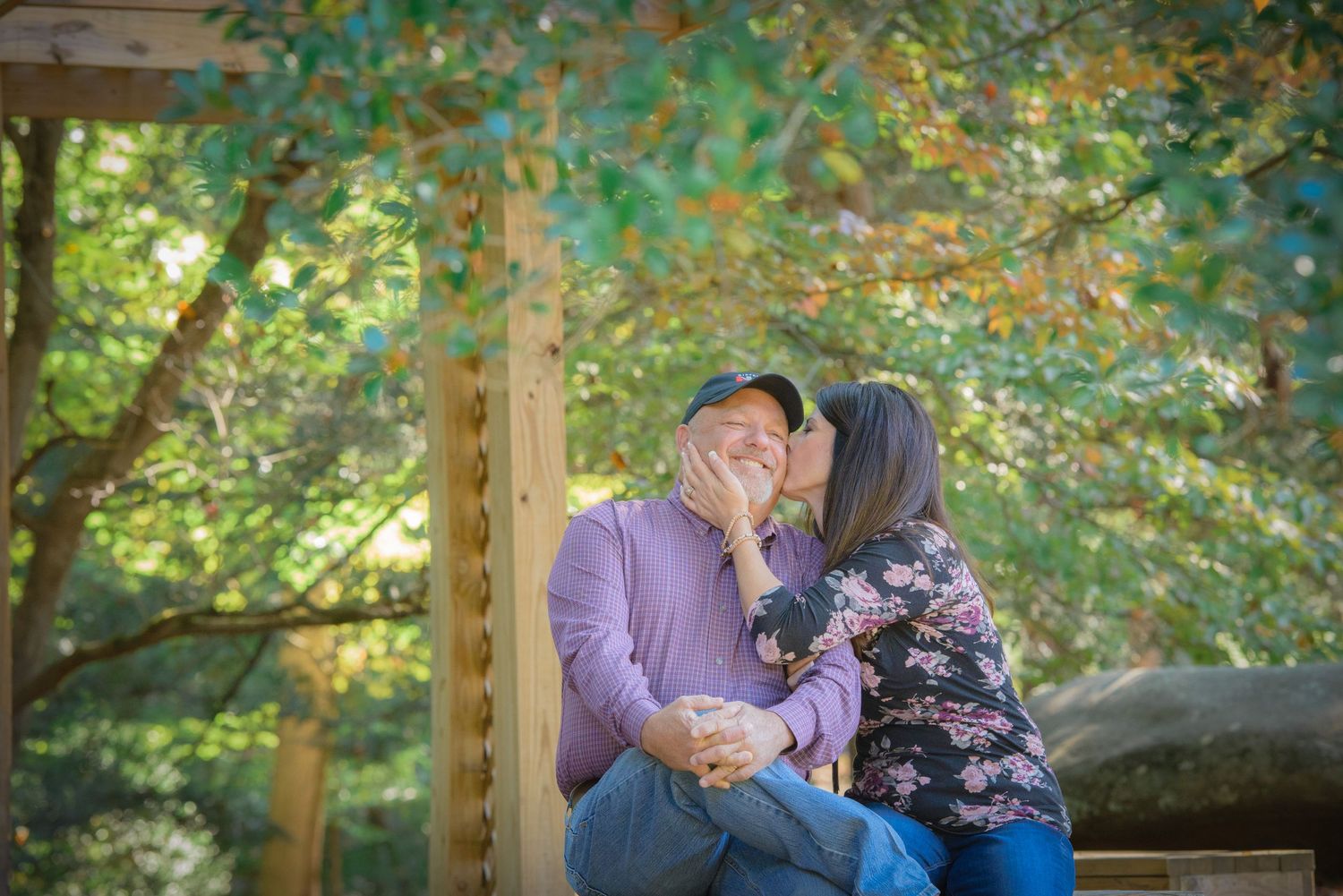 A tender romantic moment between a couple sitting on a wooden bench surrounded by lush autumn foliage by Sevierville TN Photographers.