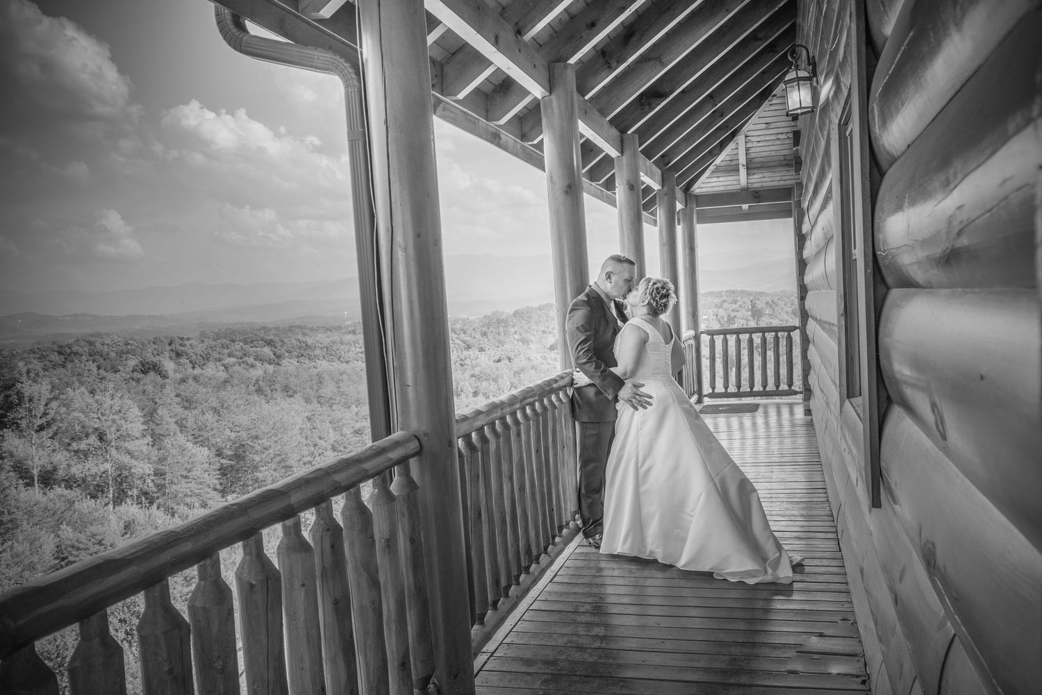 A couple in wedding attire stands together on a rustic cabin porch overlooking a scenic forested landscape in Gatlinburg TN.