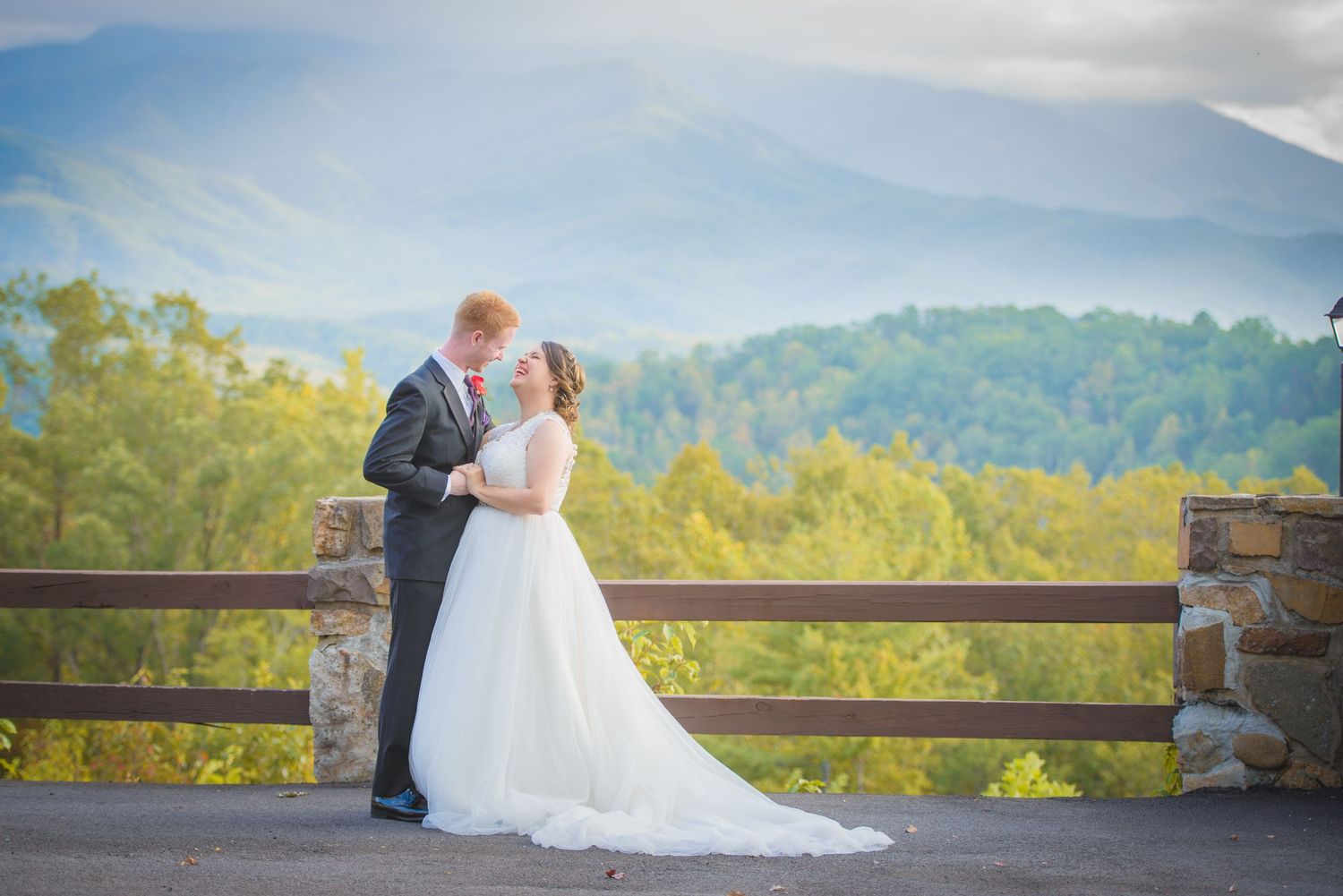 A couple shares an intimate moment on a mountain overlook with scenic misty hills and lush forest in the background in Townsend TN.