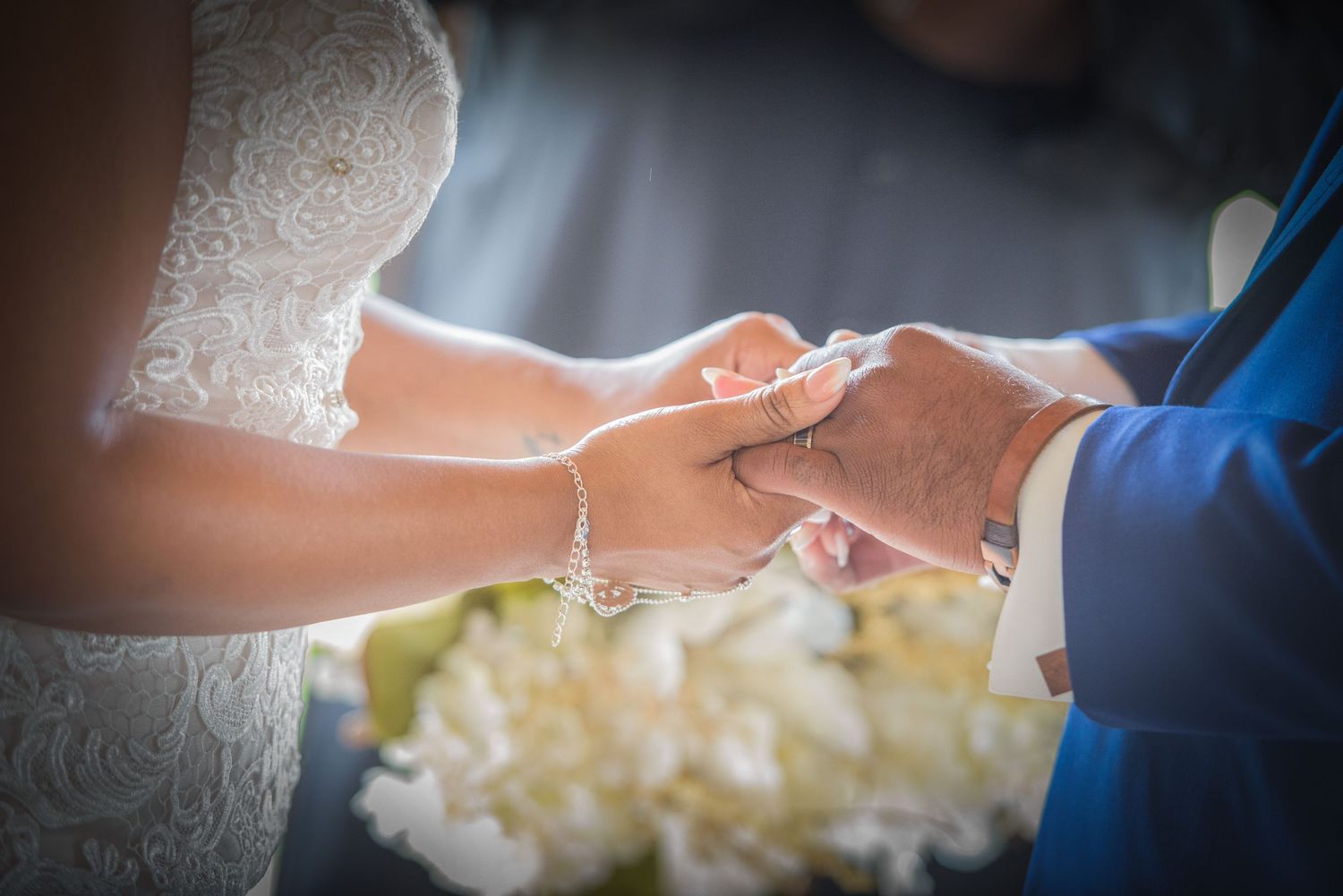 Close-up shot of newly married couple hands exchanging wedding rings with white flowers in background by Cosby Wedding Photographers.