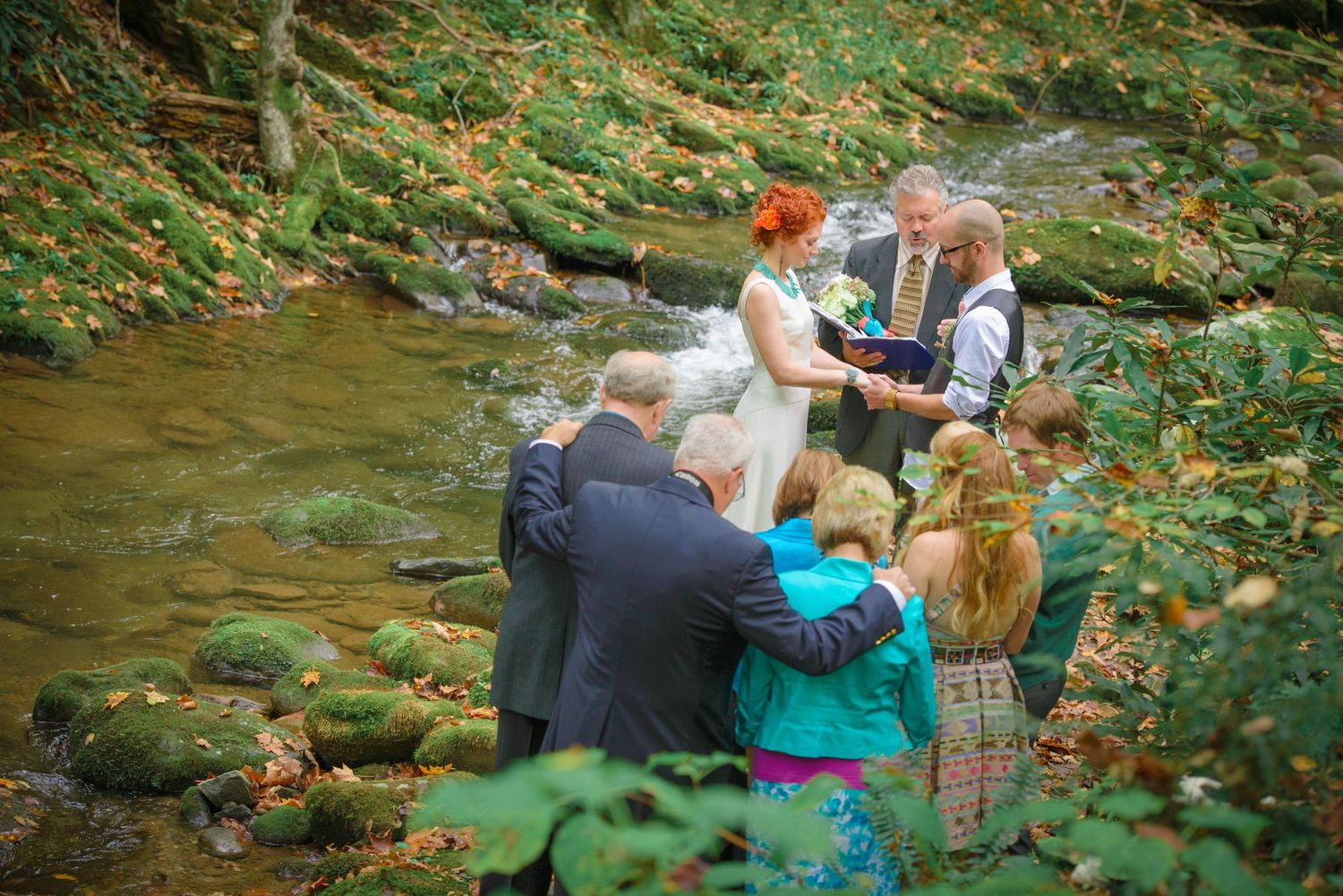 An intimate outdoor wedding ceremony takes place by a scenic creek surrounded by lush greenery and autumn foliage by Gatlinburg TN Weddings