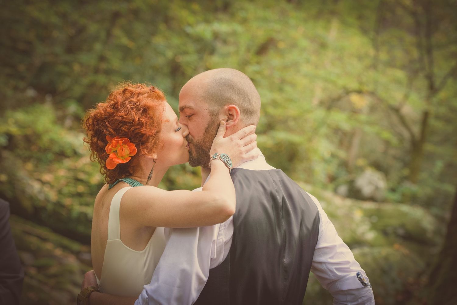 A tender outdoor embrace between a couple with vibrant red hair and a bald head in a romantic forest setting by Gatlinburg TN Weddings.