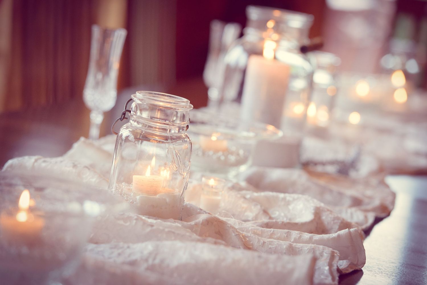 Glowing mason jar candles and champagne glasses arranged on white linens create an elegant table setting by Sevierville Photographers.