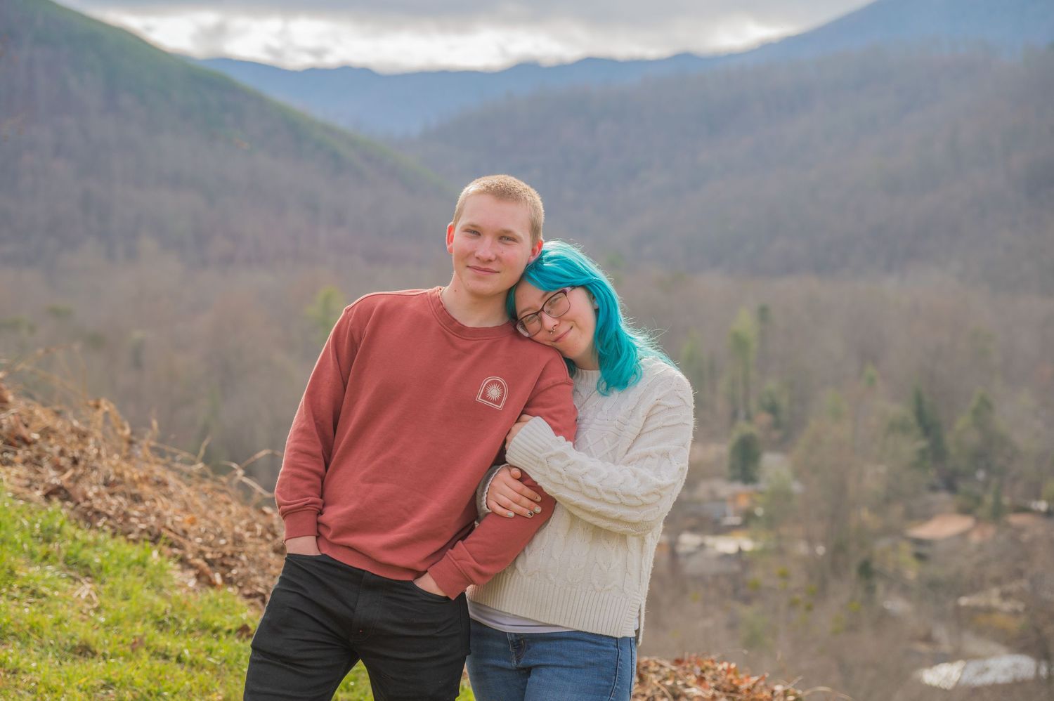 A couple poses together on a hillside scenic overlook with mountain views in the background by Sevierville TN Photographers.