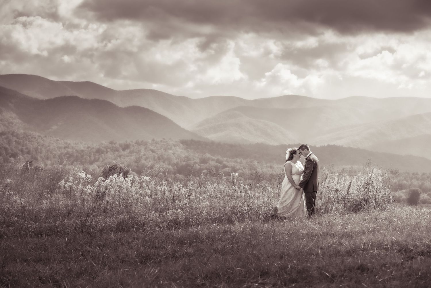 A silhouetted couple embraces on a cades cove meadow overlooking misty rolling hills in black and white by Gatlinburg Wedding Photographers.