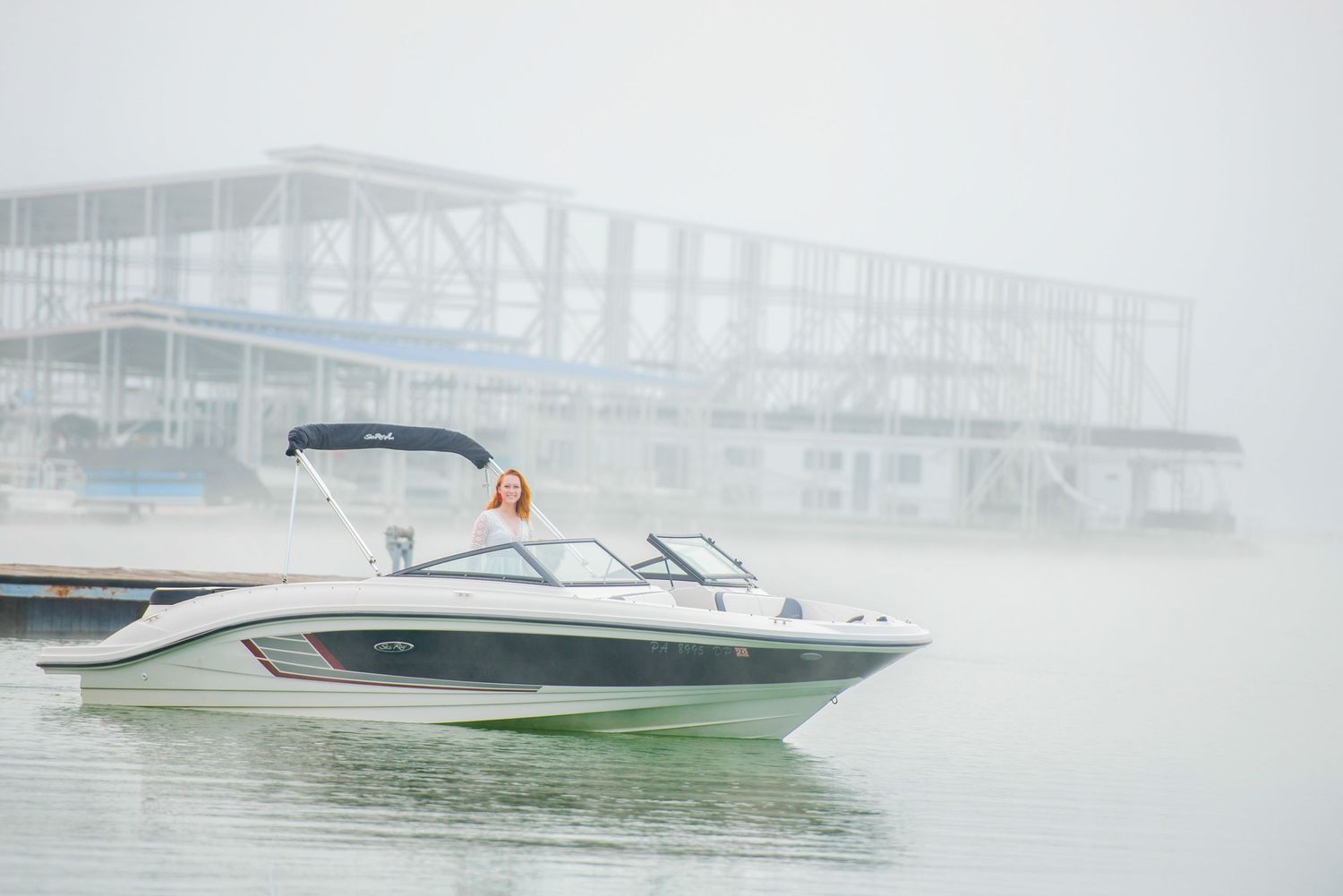 A white powerboat glides through foggy waters near a misty waterfront building structure.