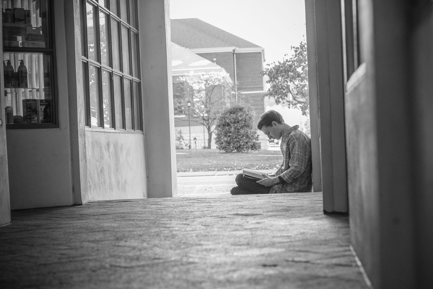 A silhouetted figure sits reading in a quiet corridor between doors, casting shadows in black and white photography.