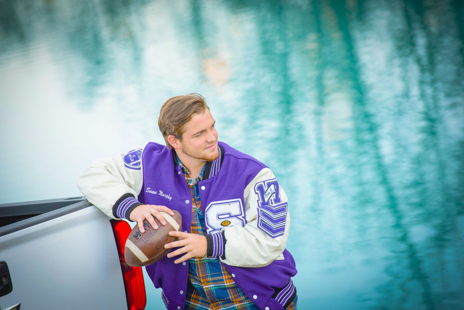 Hockey player in purple jersey sits by reflective turquoise water wearing traditional athletic gear.