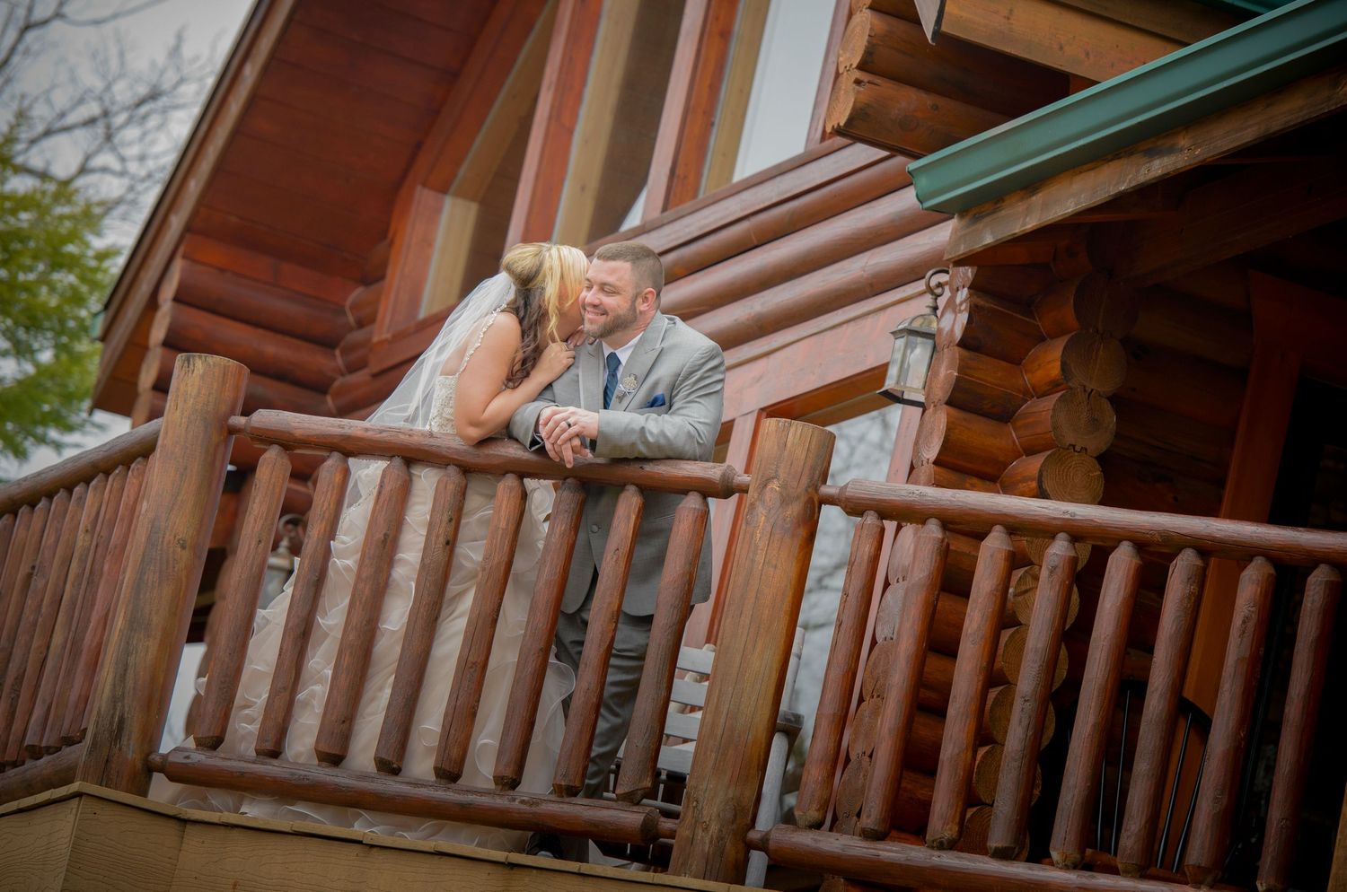 A couple shares a romantic moment on the rustic log cabin porch with wooden railings at sunset in Sevierville TN.