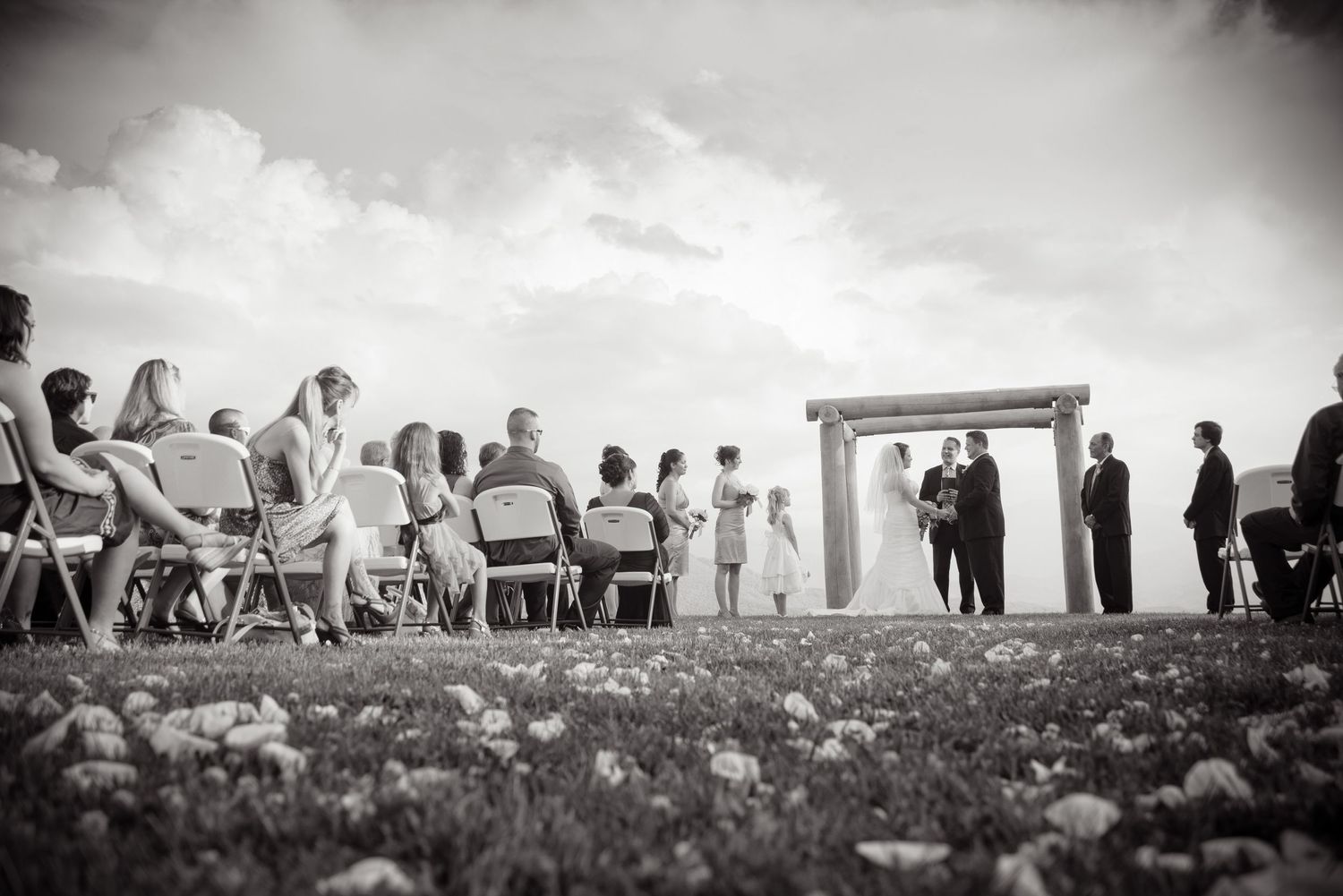 Black and white outdoor wedding ceremony with guests seated on chairs facing a decorated arch on a hilltop by Pigeon Forge Photographers.