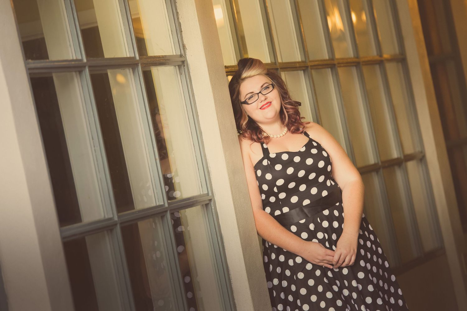 Vintage-inspired polka dot dress photographed against industrial metal window backdrop in warm lighting.