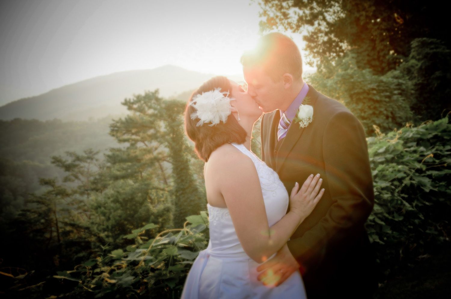 Romantic wedding couple embraces in nature with sunlight through trees and mountain backdrop at sunset in Pittman Center TN.
