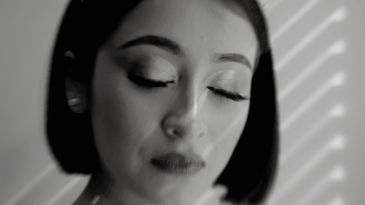 Black and white portrait in dramatic lighting shows a serene expression with closed eyes and perfect lipstick.