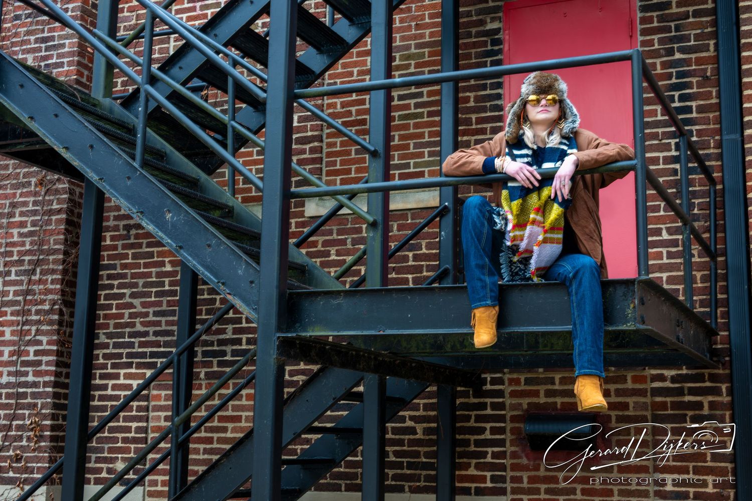 Person in casual attire sits on metal stairs against a brick wall with pink accent wall in urban setting.