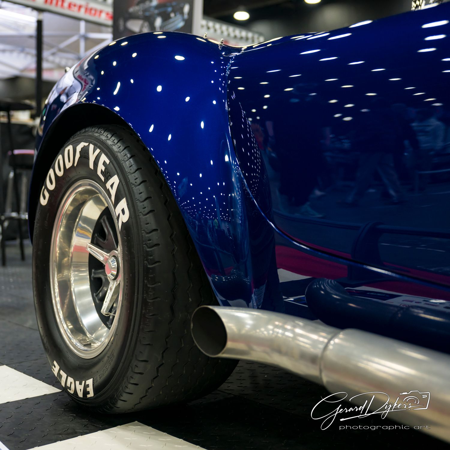 Close-up view of a classic car's chrome wheel and whitewall tire against a deep blue painted body panel.