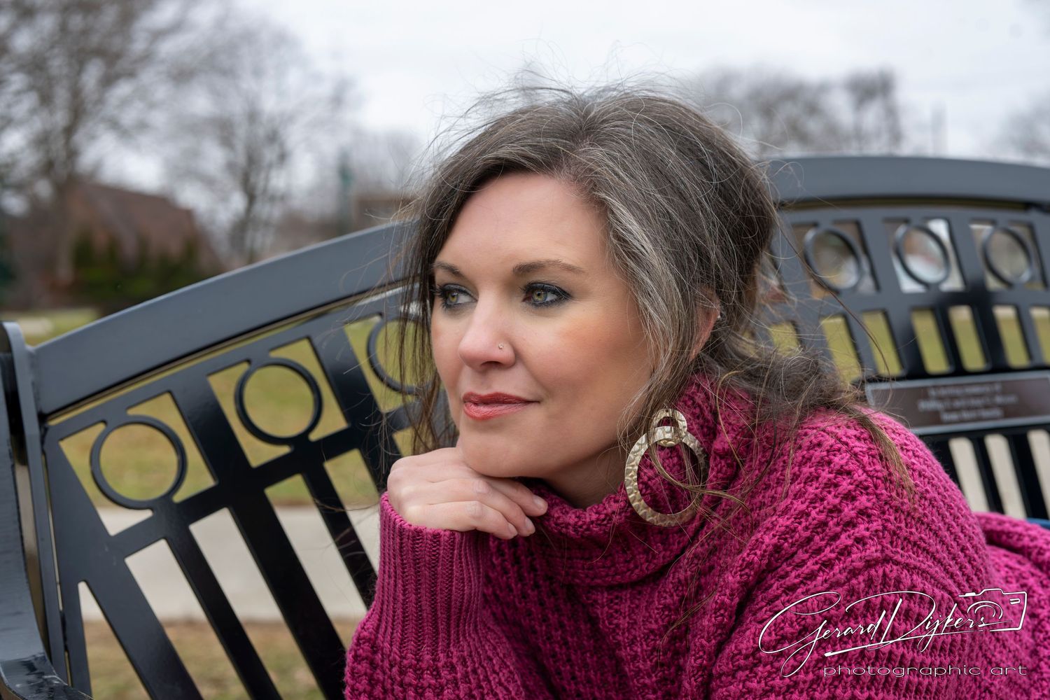 Person wearing a burgundy knit sweater poses against an ornate black metal fence in an outdoor setting.